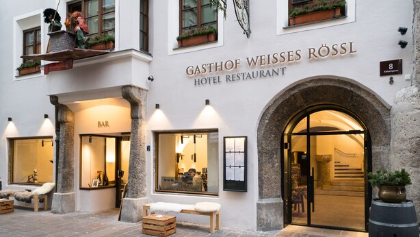 A hotel with a bar and restaurant on the ground floor, stone columns, and a stone archway entrance. - Weisses Roessl Innsbruck GmbH (Innsbruck)