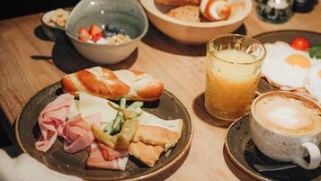 Una mesa de desayuno con diversos alimentos y un vaso de zumo de naranja.