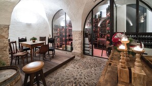 An interior with stone walls, a wooden table with chairs, a wine rack, and a red car-shaped decoration. - Weisses Roessl Innsbruck GmbH (Innsbruck)
