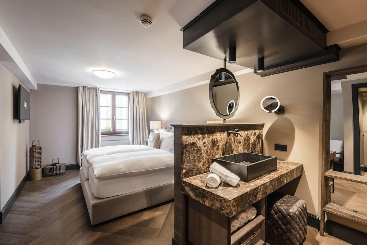 Quarto de hotel com cama, toucador de mármore, espelho grande e janela com cortinas.