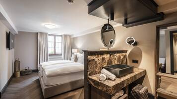 Habitación de hotel con cama, tocador de mármol, un espejo grande y una ventana con cortinas.