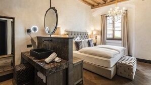 A bedroom with a large bed, a vanity with a mirror, a chandelier, and a window with curtains. - Weisses Roessl Innsbruck GmbH (Innsbruck)