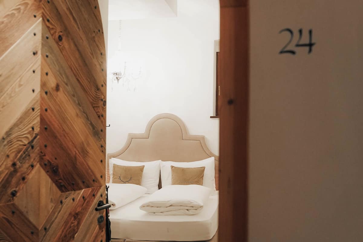 Quarto de hotel com porta de madeira, cama com roupa de cama branca e o número '24' na parede.