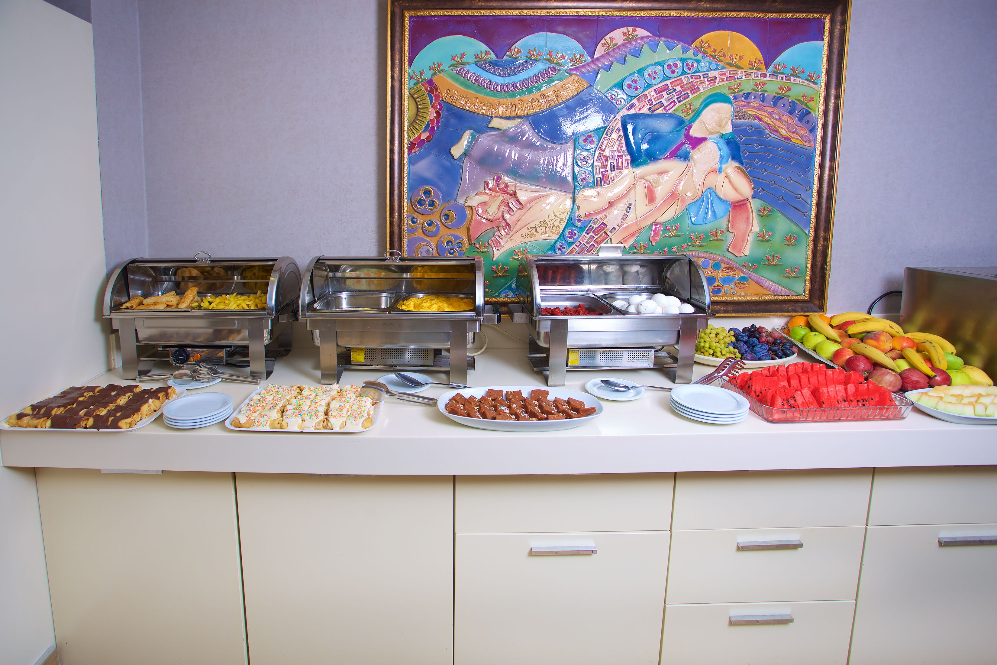 A buffet with various food items and a colorful painting on the wall.