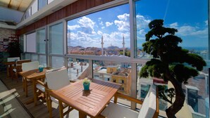 A balcony with wooden furniture and a bonsai tree, overlooking a cityscape with a prominent tower and a clear blue sky. - Zagreb Hotel (Istanbul)