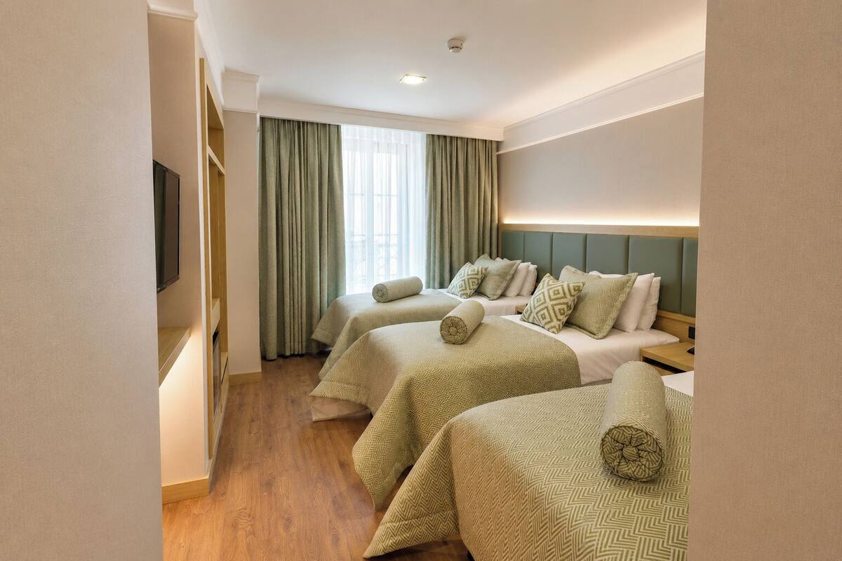A hotel room with two beds, a television, a window with curtains, and a wooden floor.
