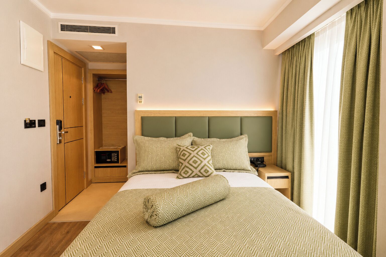 Habitación de hotel con cama, mesitas de noche, armario y ventana con cortinas.