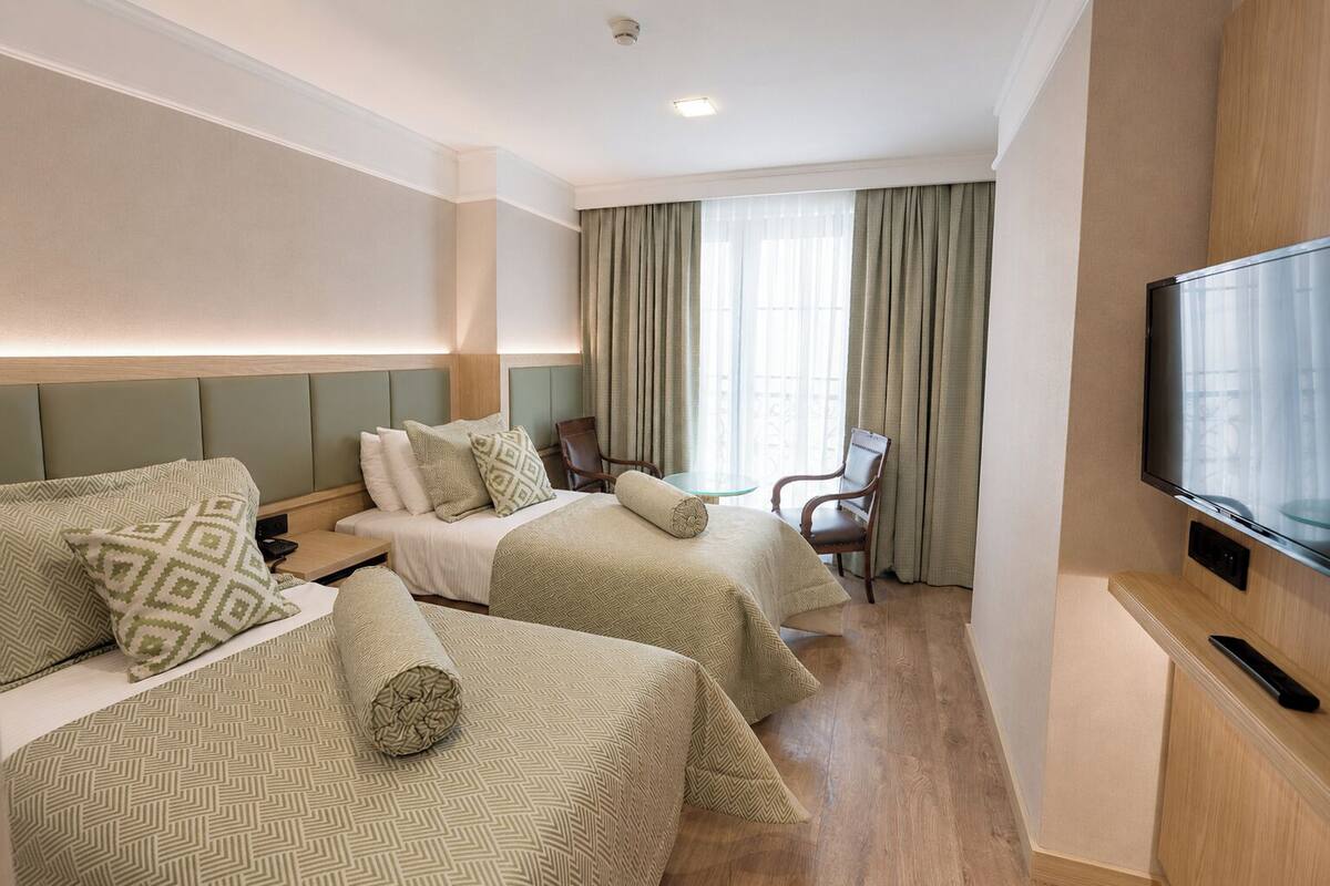 A hotel room with two beds, a TV, a chair, and a small table.