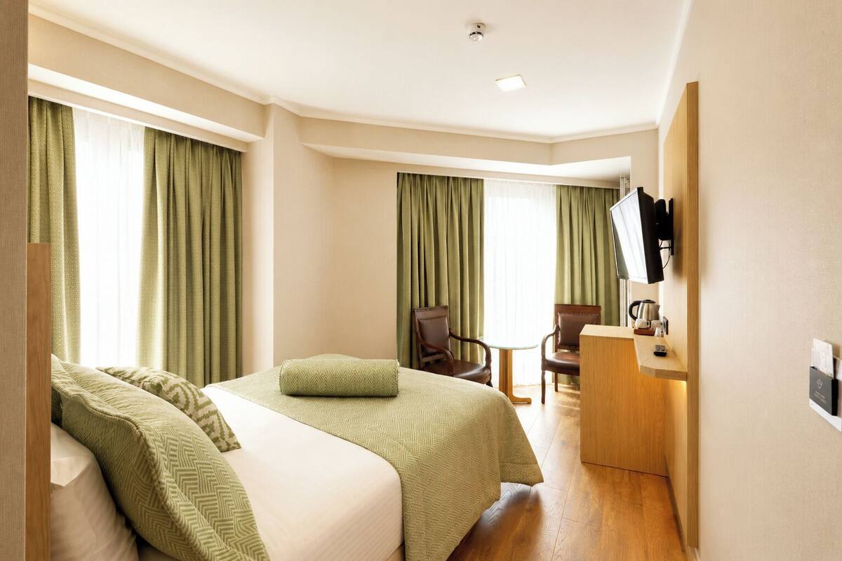 A hotel room with two beds, a desk, chairs, a television, and a small table.
