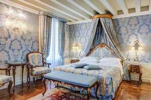 Un dormitorio con cama a dosel, una zona de estar con un banco y dos mesitas de noche con lámparas.