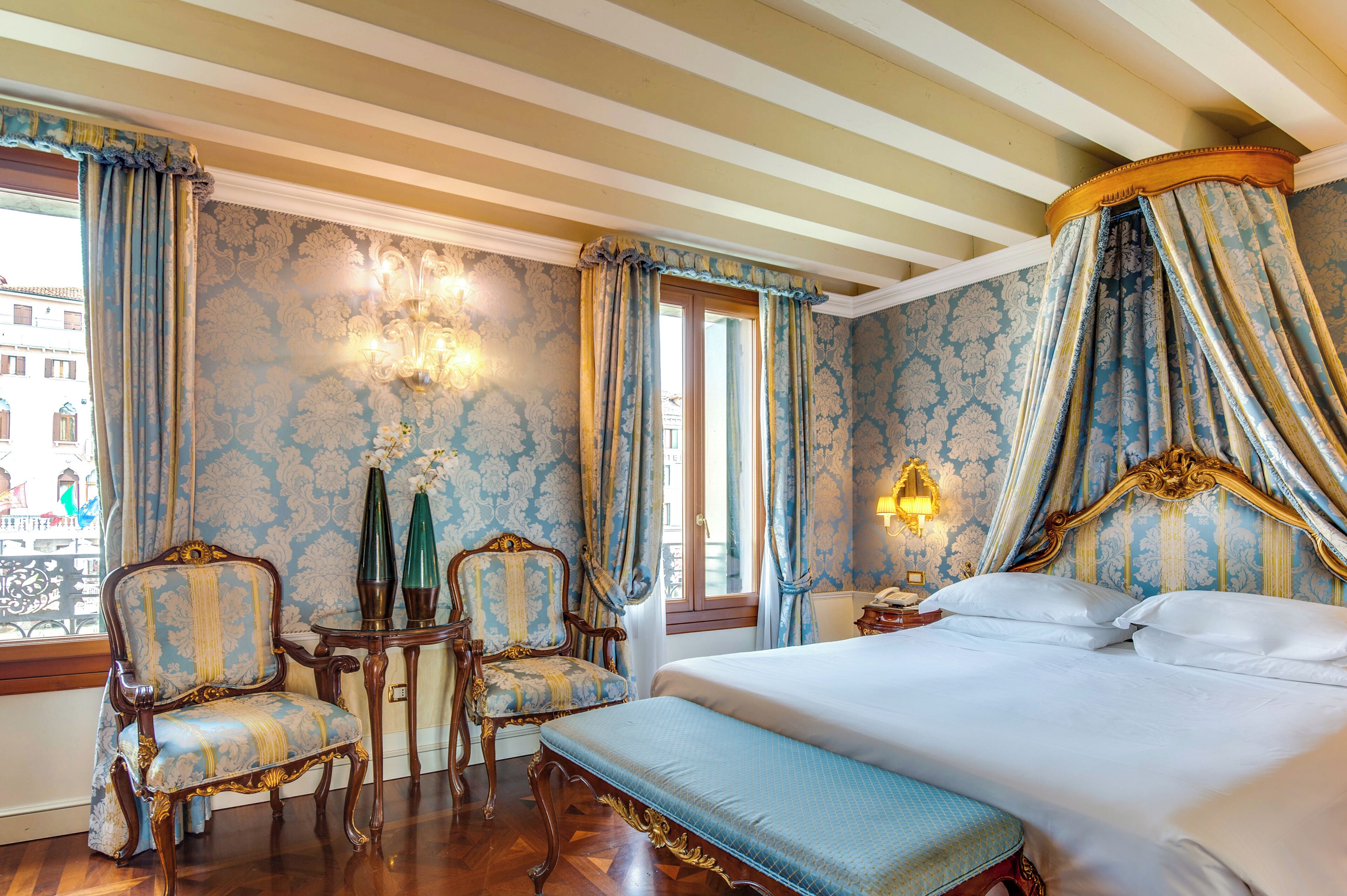 Ein klassisch eingerichtetes Zimmer mit einem großen Bett, zwei Stühlen, einem kleinen Tisch und einem Baldachin.