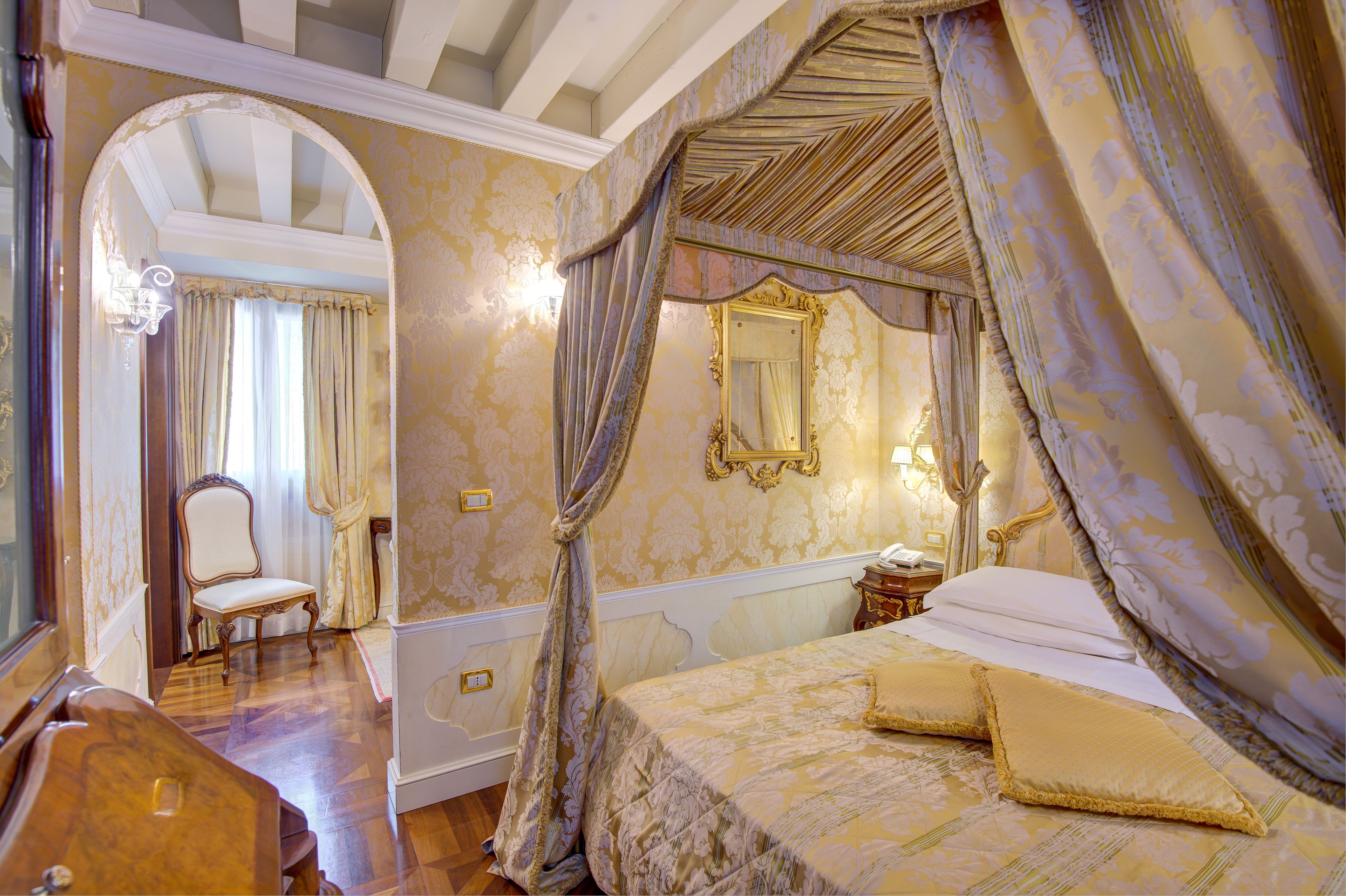 A luxurious bedroom with a canopy bed, ornate mirror, and classic furniture.