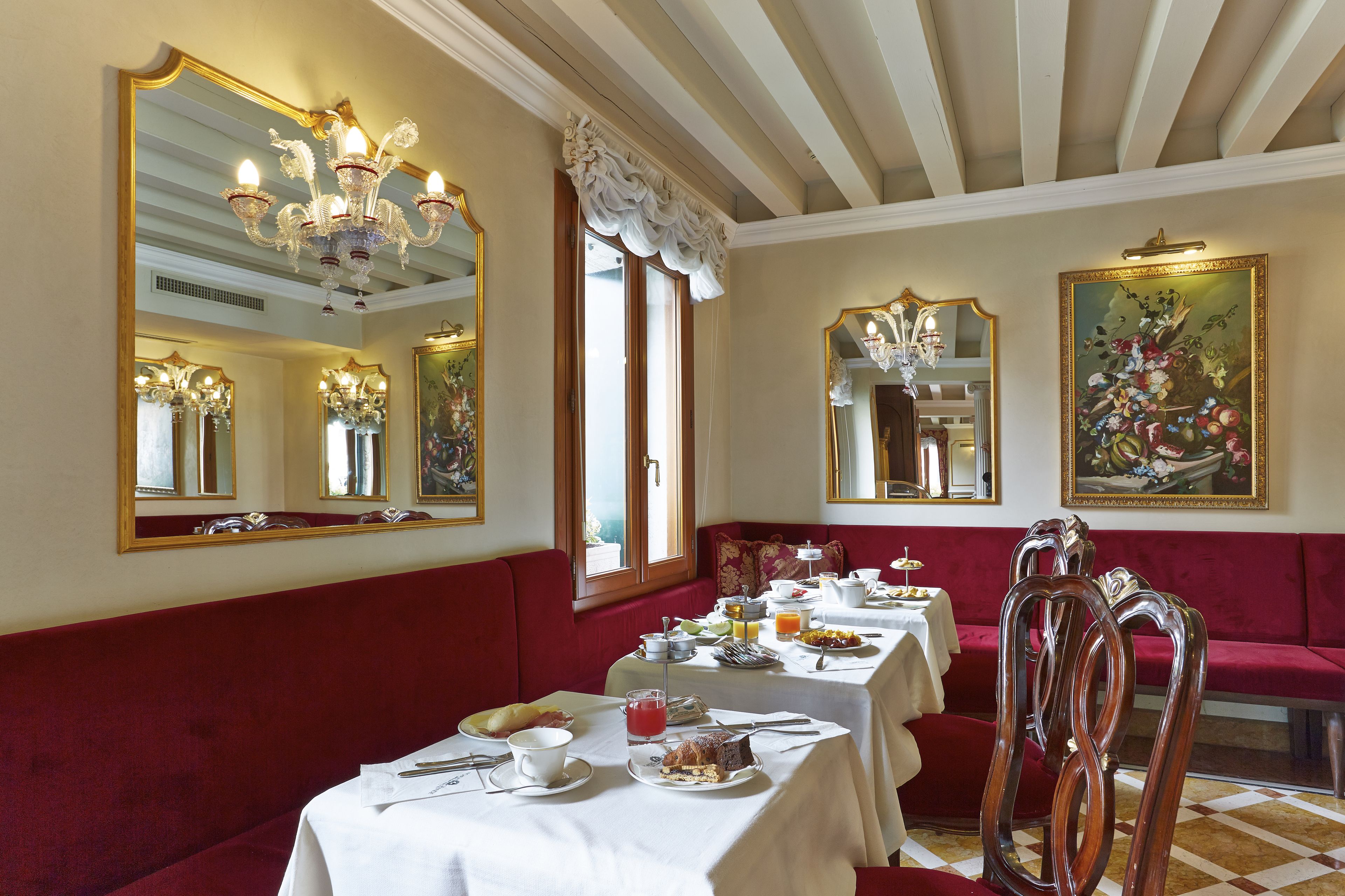 A dining area with red upholstered booths, white tablecloths, and ornate chandeliers.