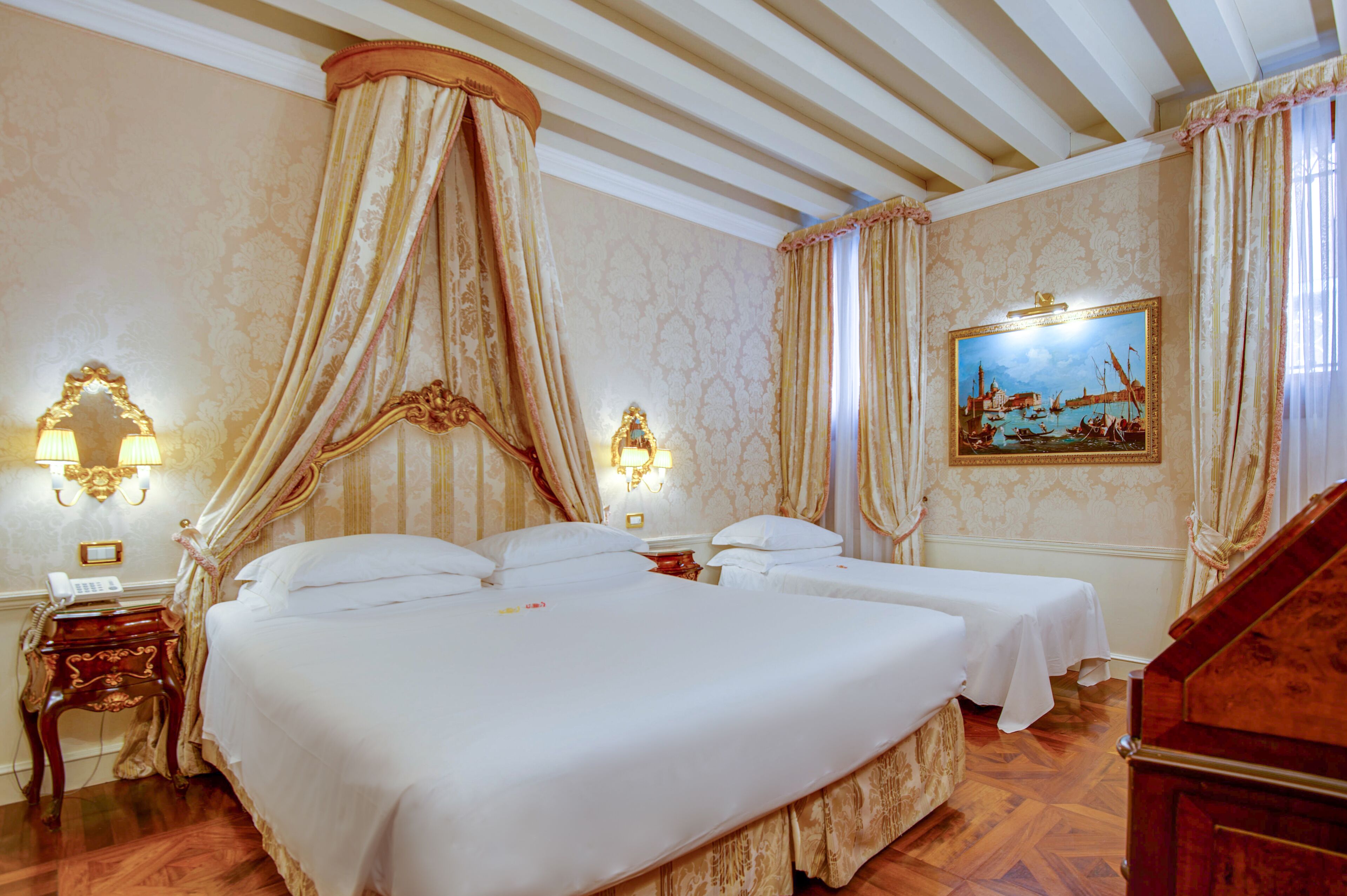 A hotel room with a large bed, two bedside tables, a nightstand, a canopy bed, a painting, and a wooden staircase.
