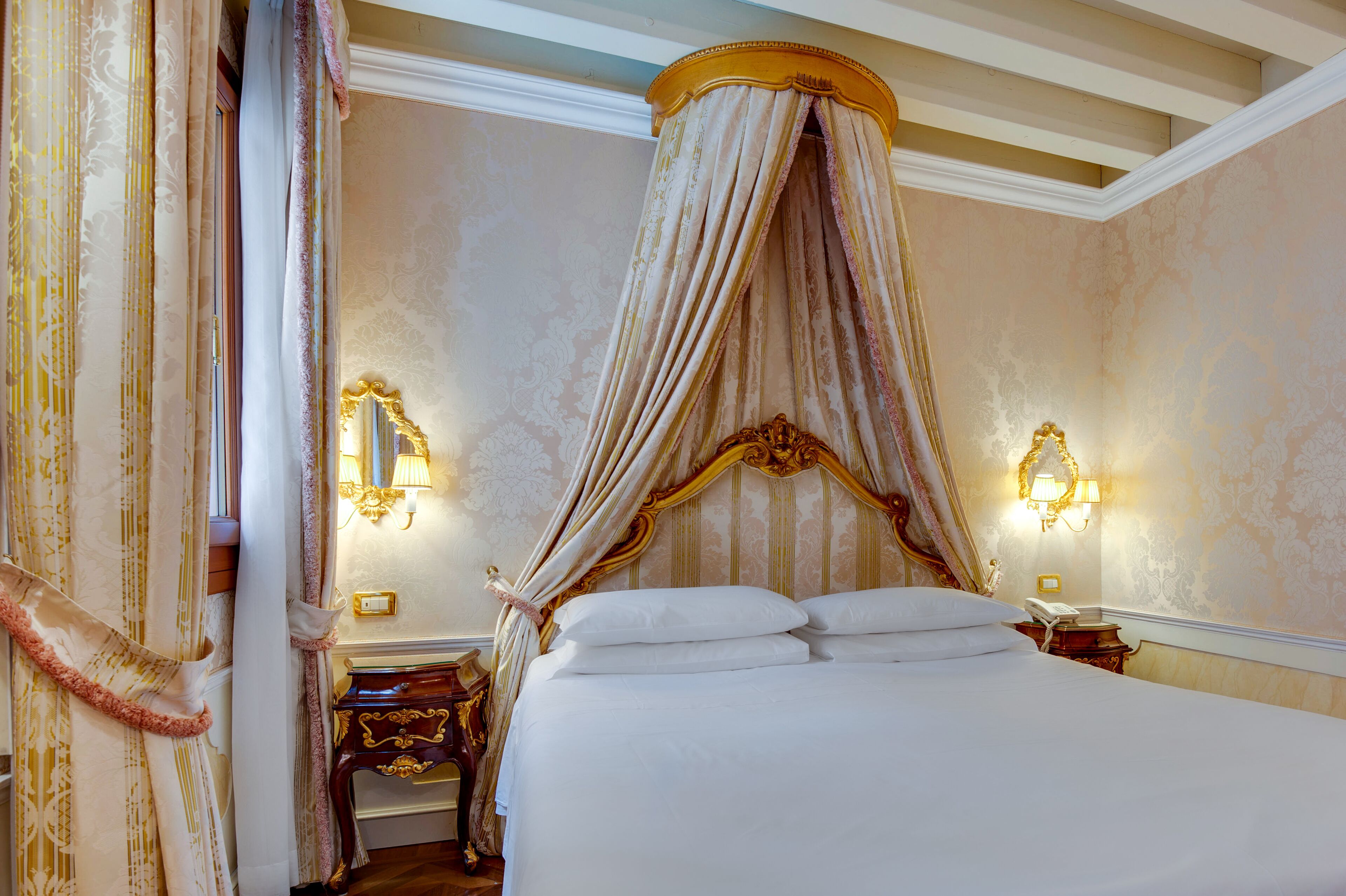 A luxurious bedroom with a canopy bed, ornate wall sconces, and a classic design.