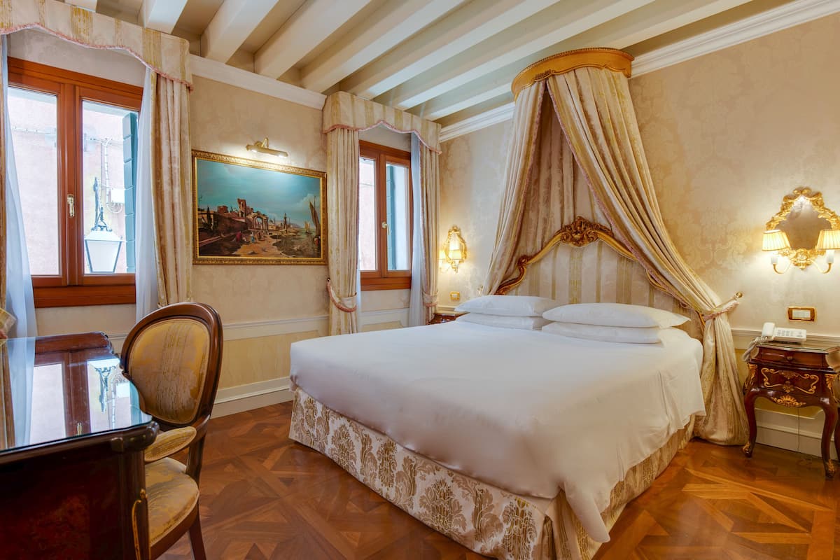 A bedroom with a large bed, a wooden chair, a desk, and a painting on the wall.