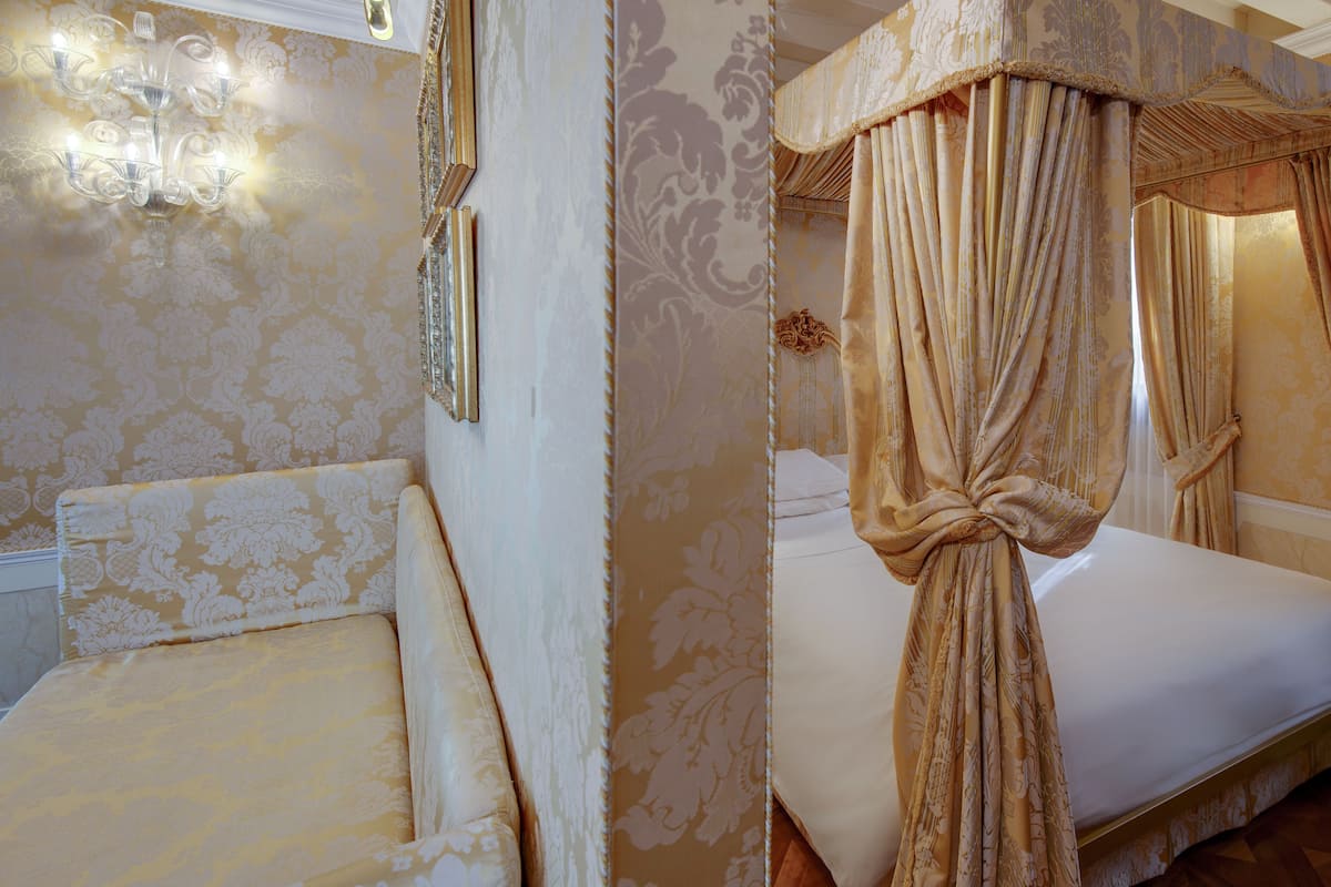 A room with a bed, a chandelier, and ornate wallpaper.