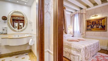 Una habitación de hotel con una cama grande, un tocador con espejo, un cuadro en la pared y una alfombra roja estampada.