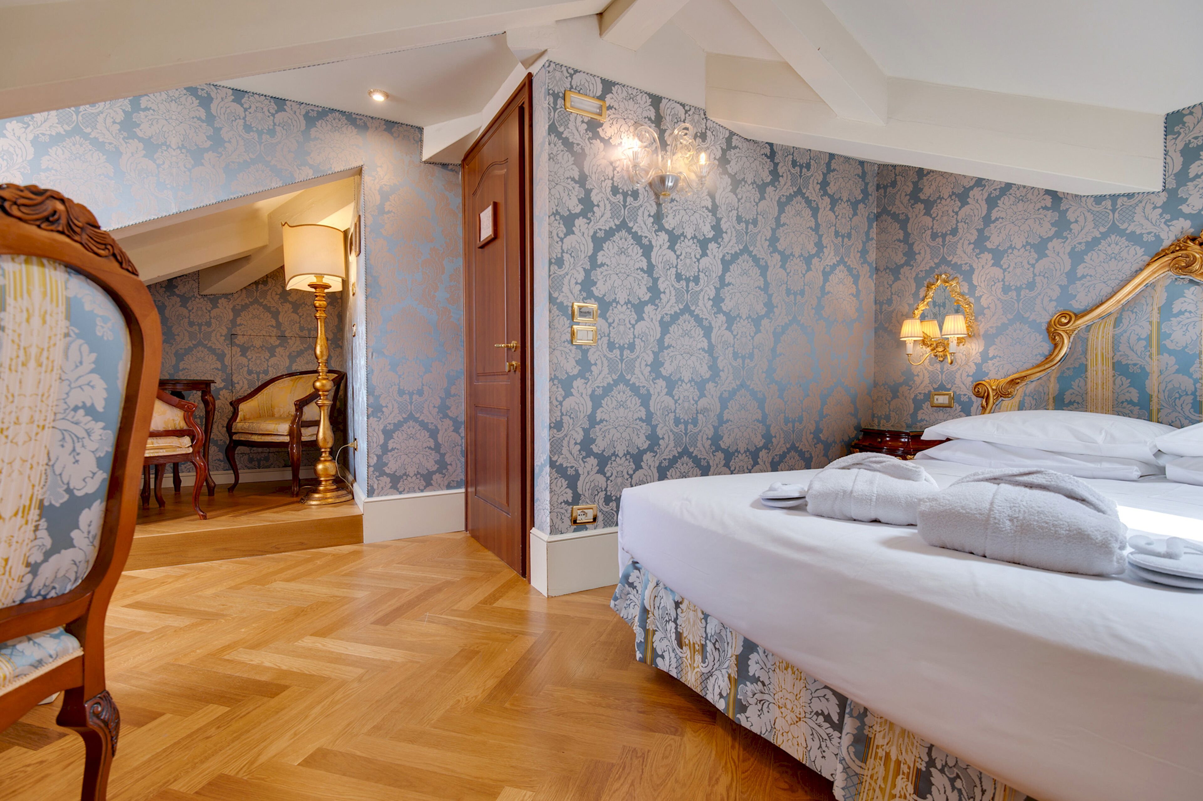 A bedroom with a large bed, a wooden chair, a desk, and a lamp.