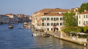 A canal with boats, historic buildings, and a waterfront café. - Hotel Canal Grande (Venice)