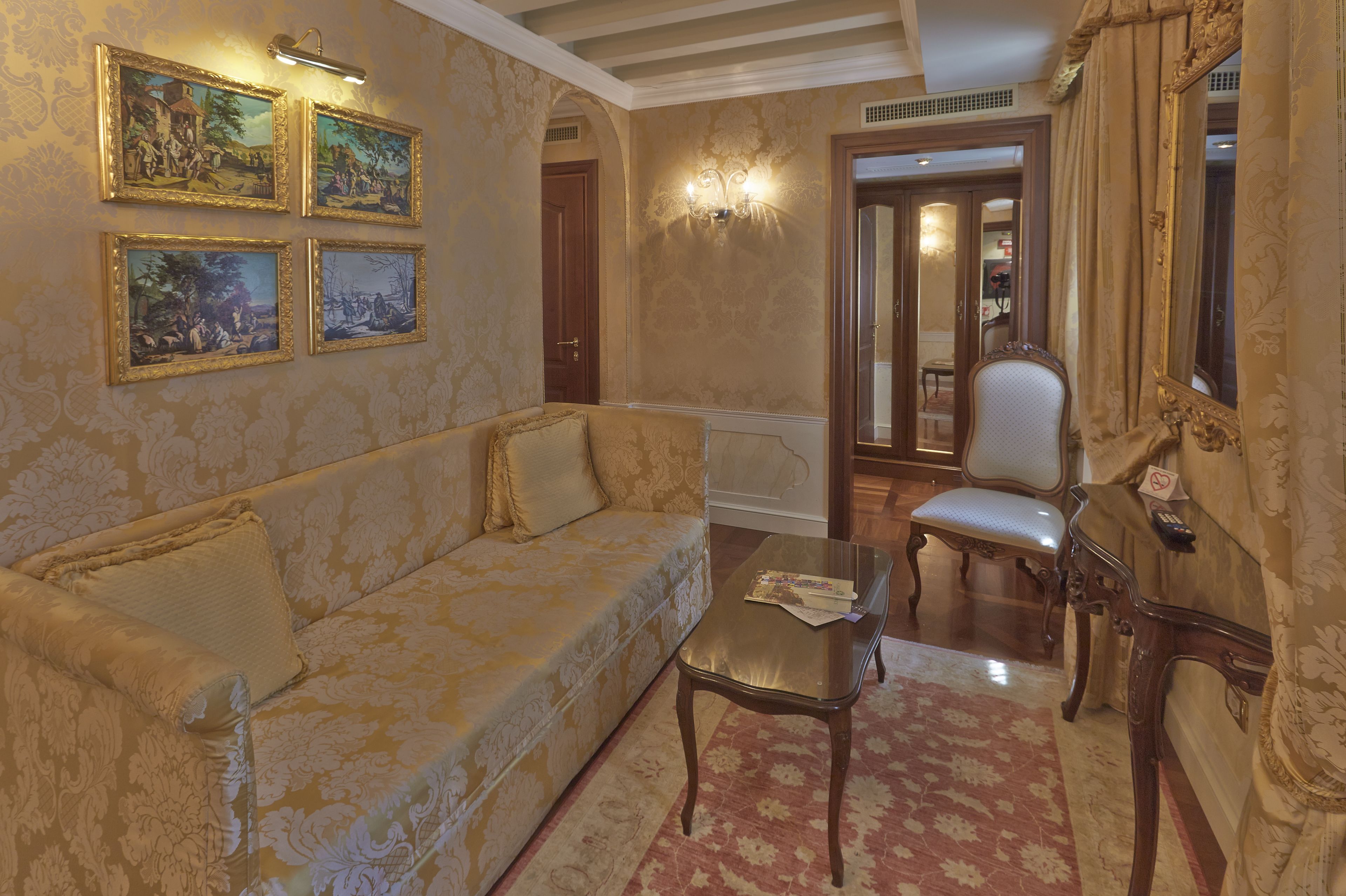 A room with a sofa, a table, a chair, and wall-mounted paintings.
