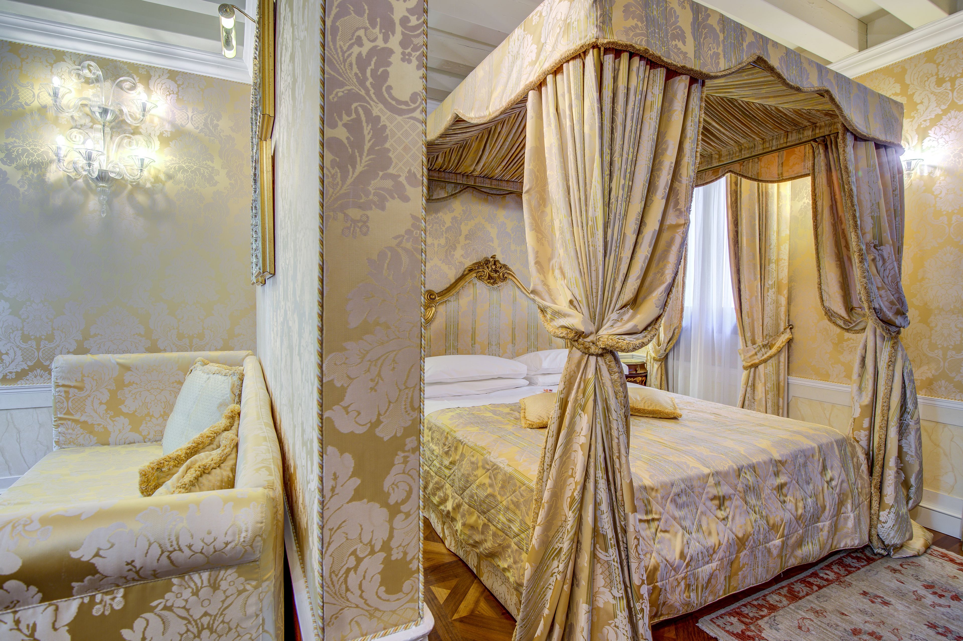 Een hemelbed met uitgebreide draperieën, een comfortabele bank en een kroonluchter in een rijk ingerichte kamer.