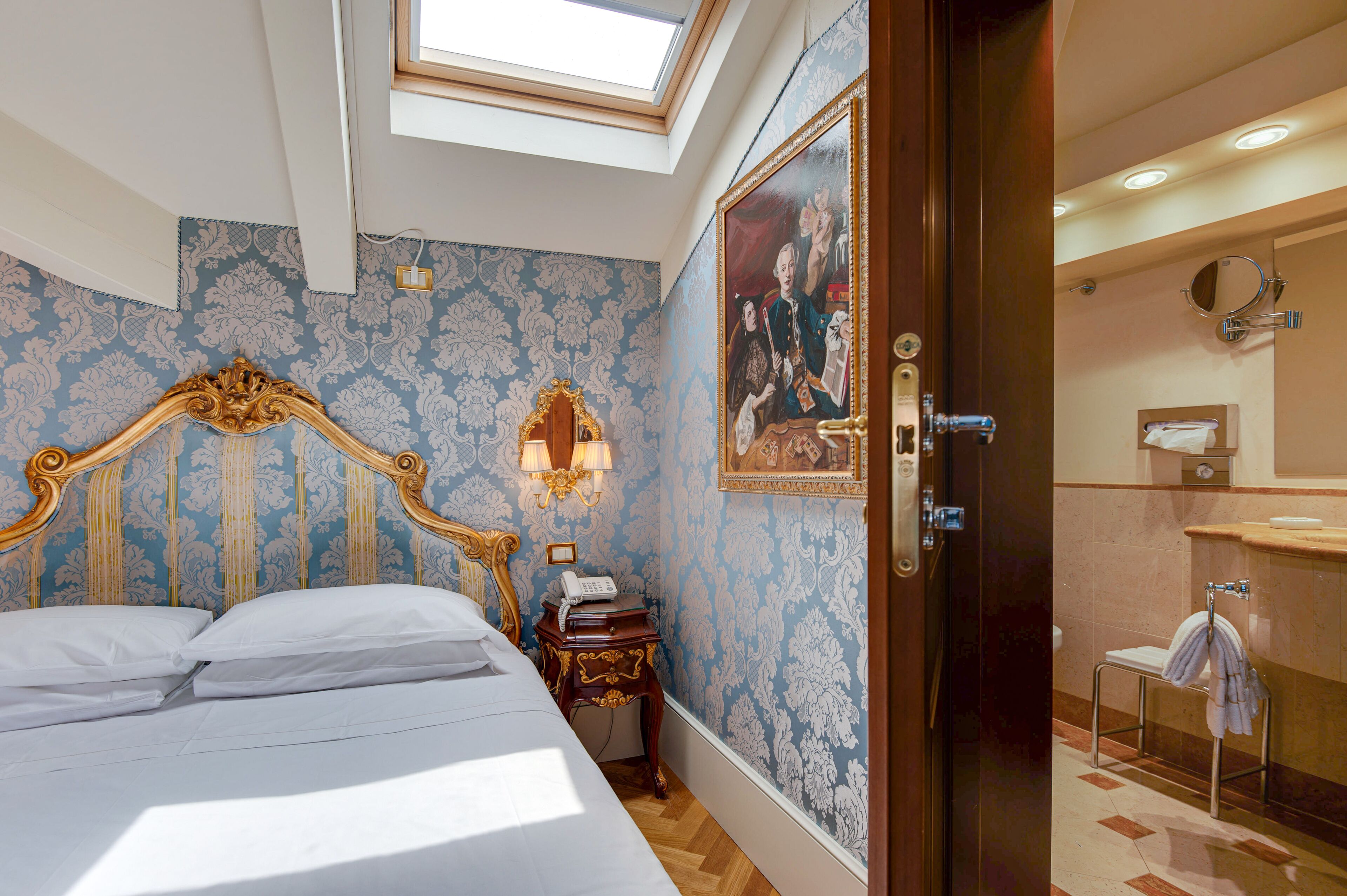 Een hotelkamer met een groot bed, een nachtkastje met een lamp, een schilderij aan de muur en een badkamer met een wastafel en spiegel.