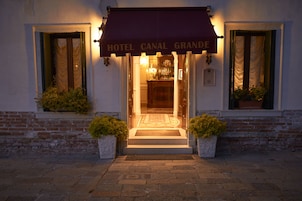 The entrance of Hotel Canal Grande with a welcoming awning and steps leading up to the door.