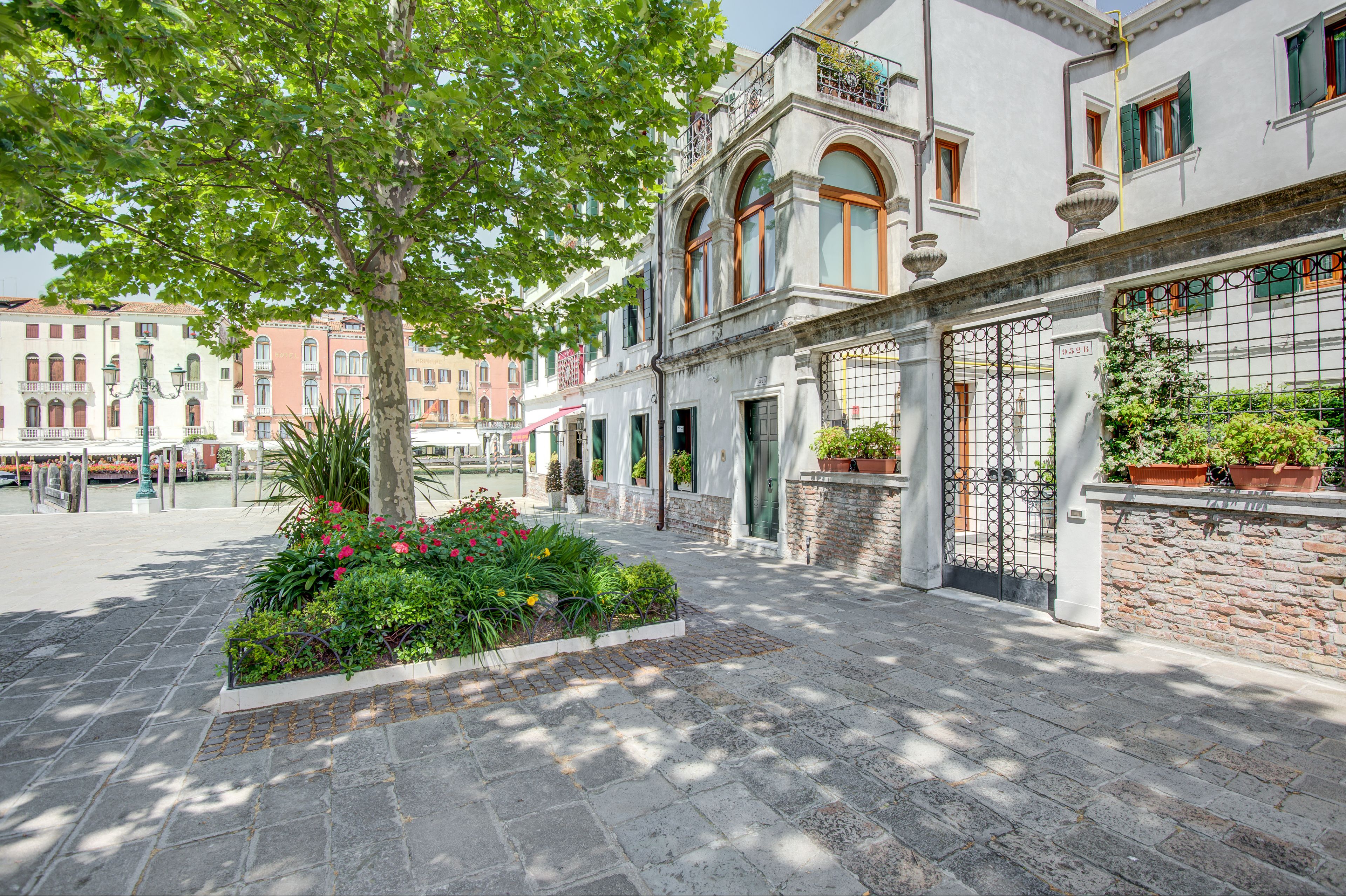 A courtyard with a tree, flower beds, and a building with a stone wall and metal gate.