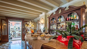 A bar area with a checkered floor, a bar counter with a variety of bottles, and a view of a building outside. - Hotel Canal Grande (Venice)