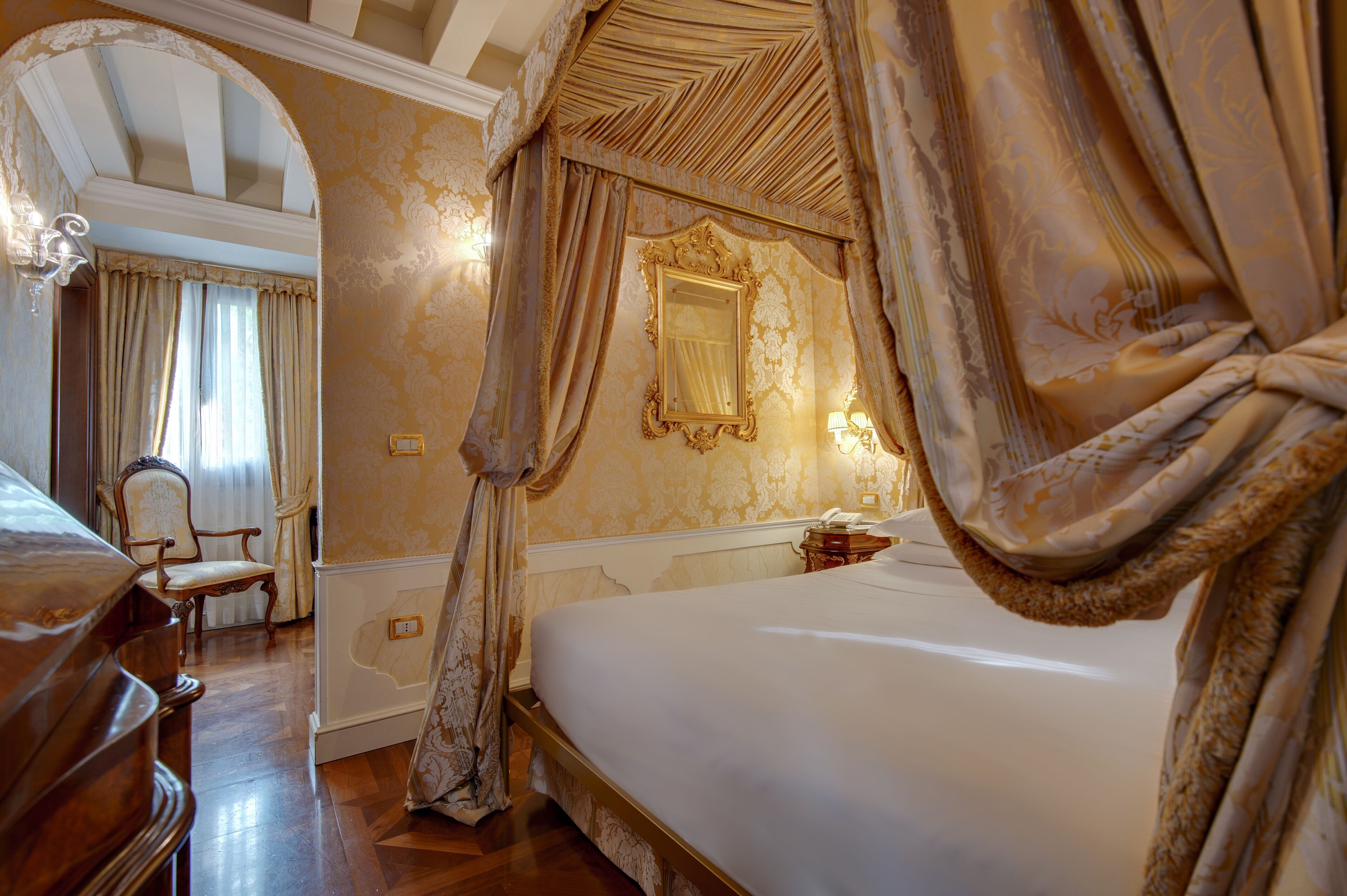 A luxurious bedroom with a large bed, ornate curtains, and a classic mirror.