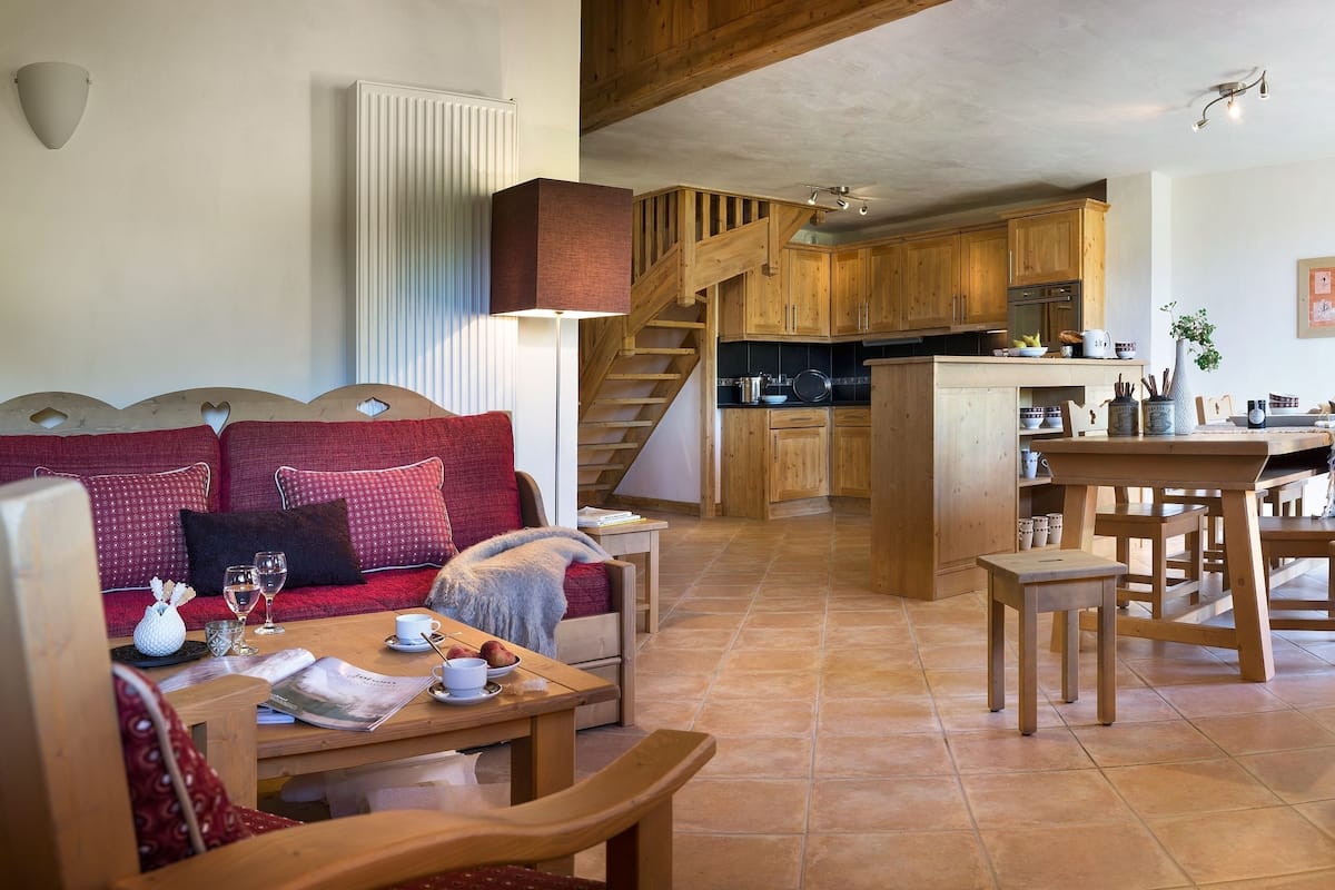 Un salon chaleureux avec un canapé, une table à manger et un coin cuisine doté de meubles en bois et d’un escalier.