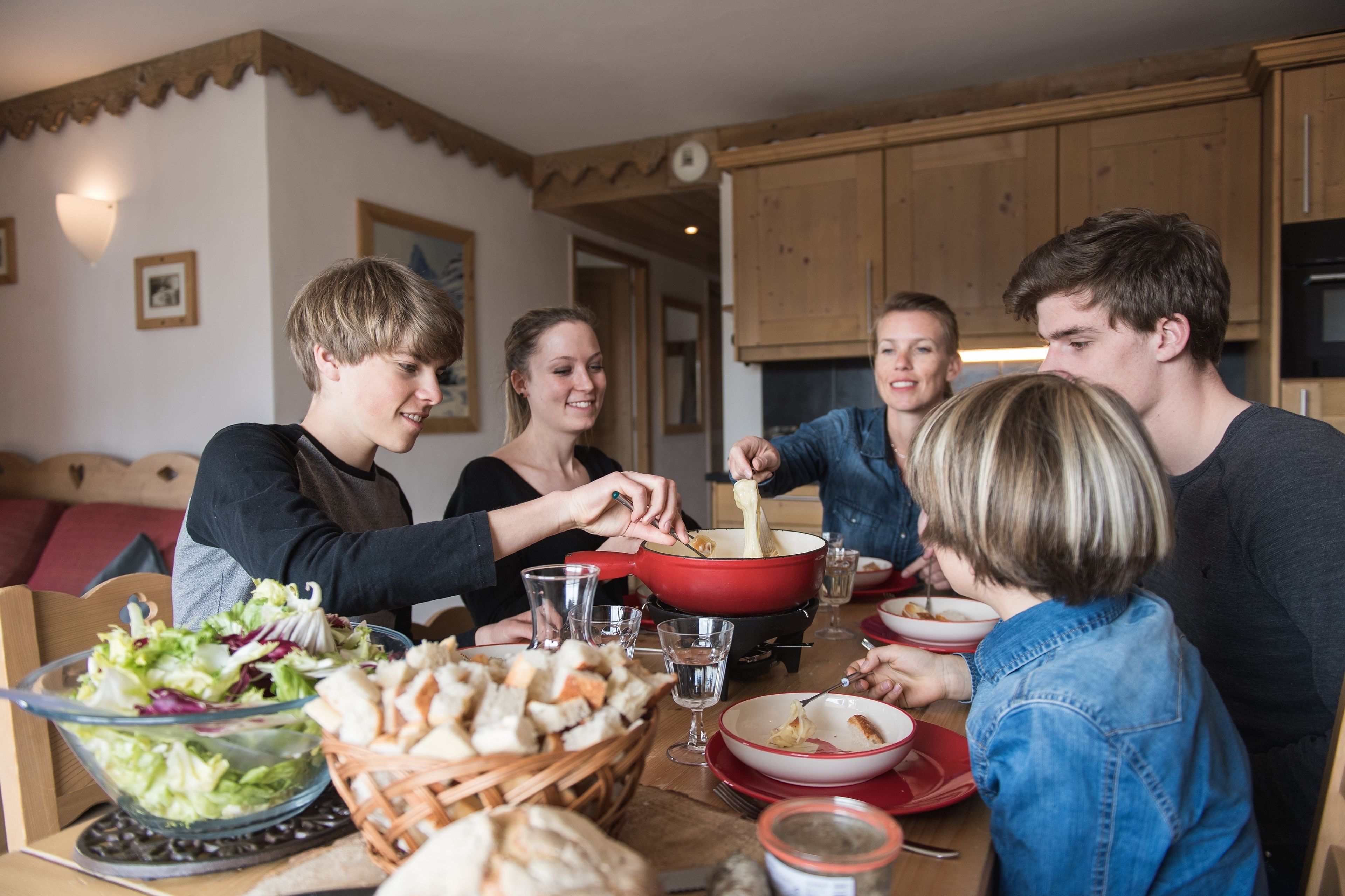A family dining together at a wooden table with a red pot, salad, and bread.
