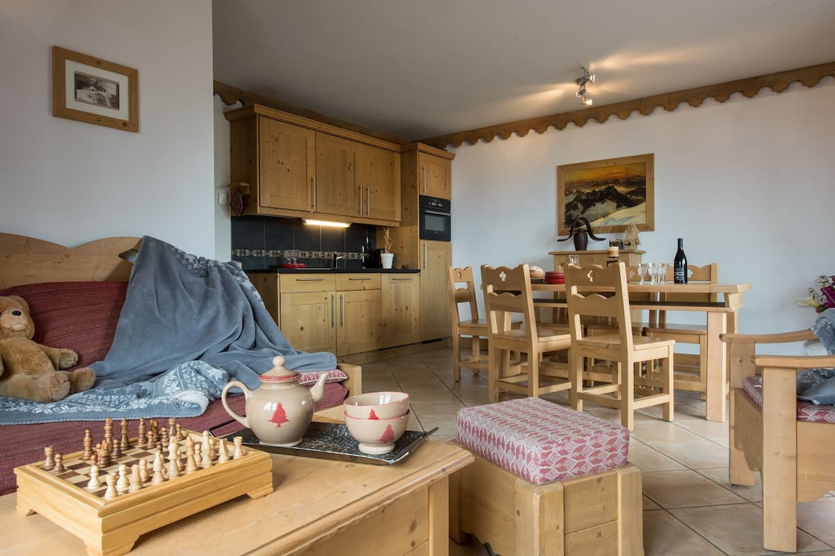 Un salon chaleureux avec un canapé en bois, un jeu d’échecs et un coin repas doté de meubles en bois.