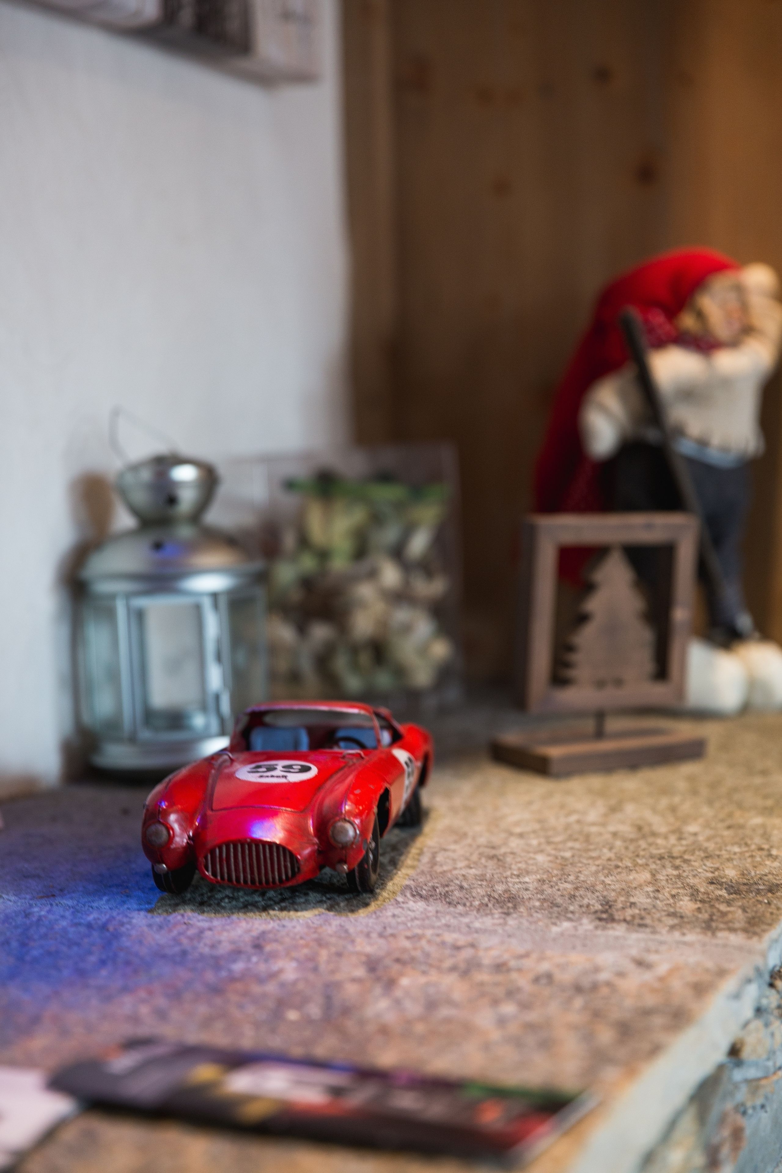 A model car on a shelf with a metal lantern and a framed picture in the background.