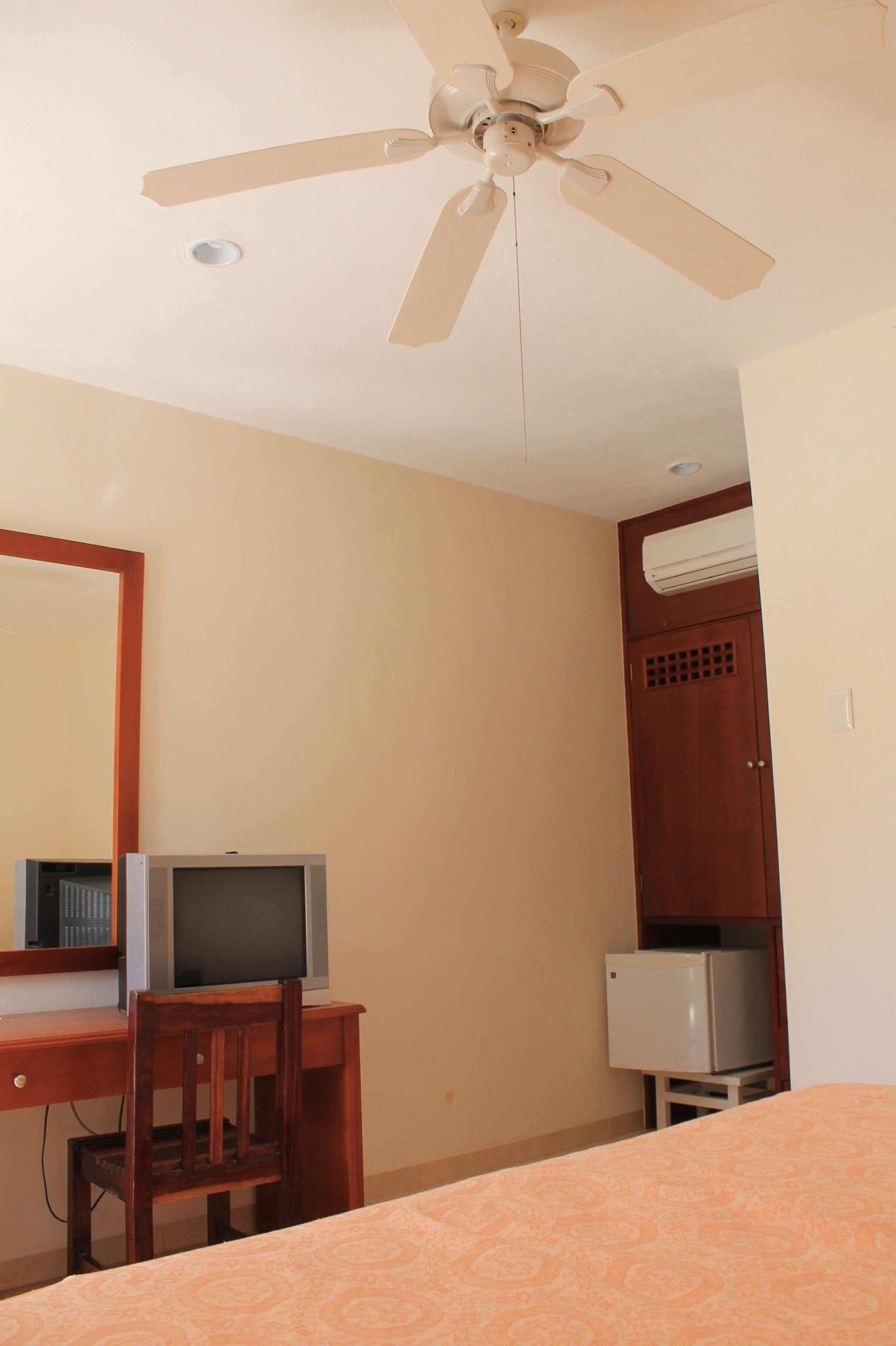 Camera d'albergo con un letto, una scrivania con computer e una sedia, una ventola a soffitto e un condizionatore d'aria.