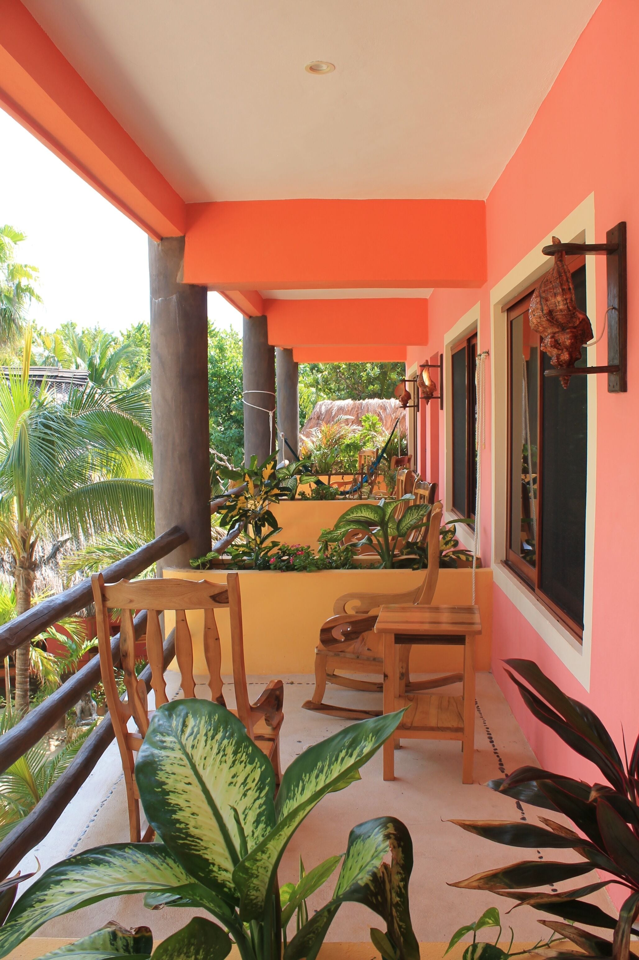 Een balkon met houten stoelen, plantenpotten en uitzicht op palmbomen.