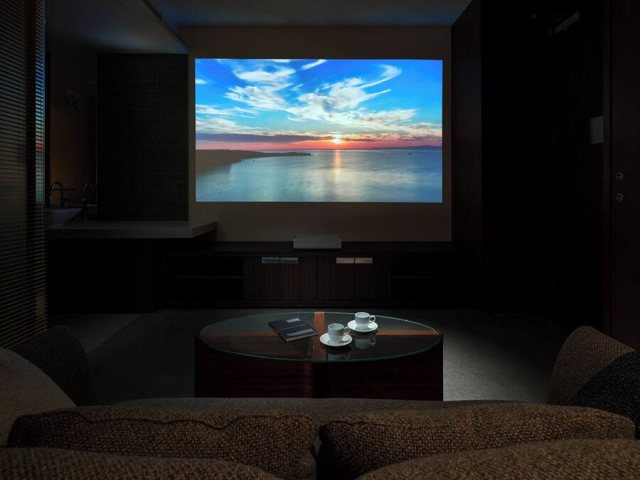 A modern living room with a large flat-screen TV displaying a sunset over water, a coffee table with cups, and a cozy seating area.