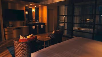 A modern hotel room with a large bed, a sitting area with a small table, a wicker basket, a large mirror, a TV, and a view of the city through a large window.