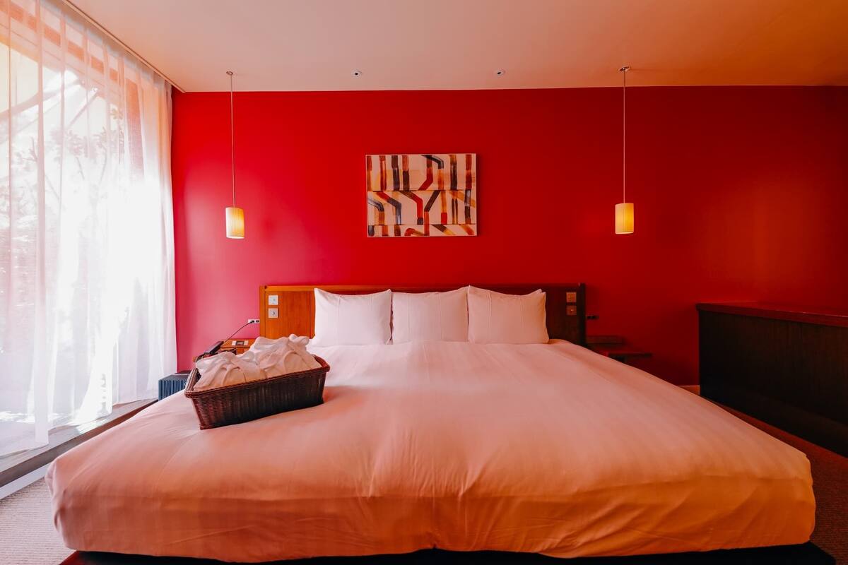 A large bed with white linens, a red wall, and a painting.