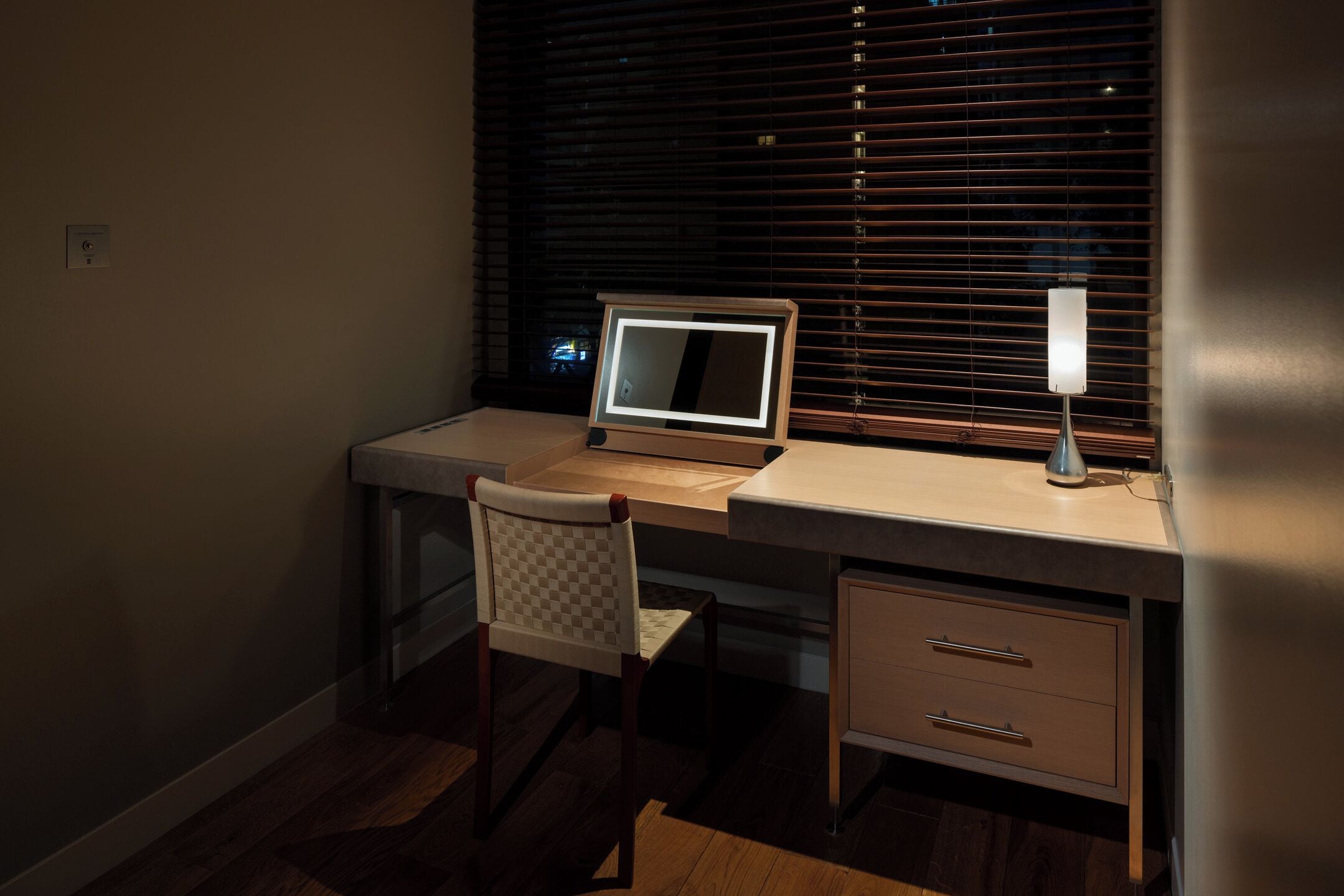 A modern desk with a laptop, a chair, and a desk lamp.