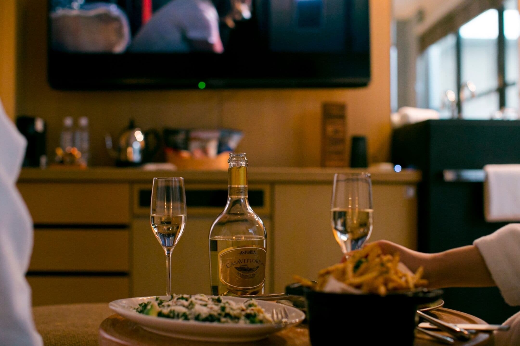 Ein Esstisch mit einer Flasche Asti Rosso, zwei Weingläsern, einem Teller mit Essen und einem Korb Pommes.