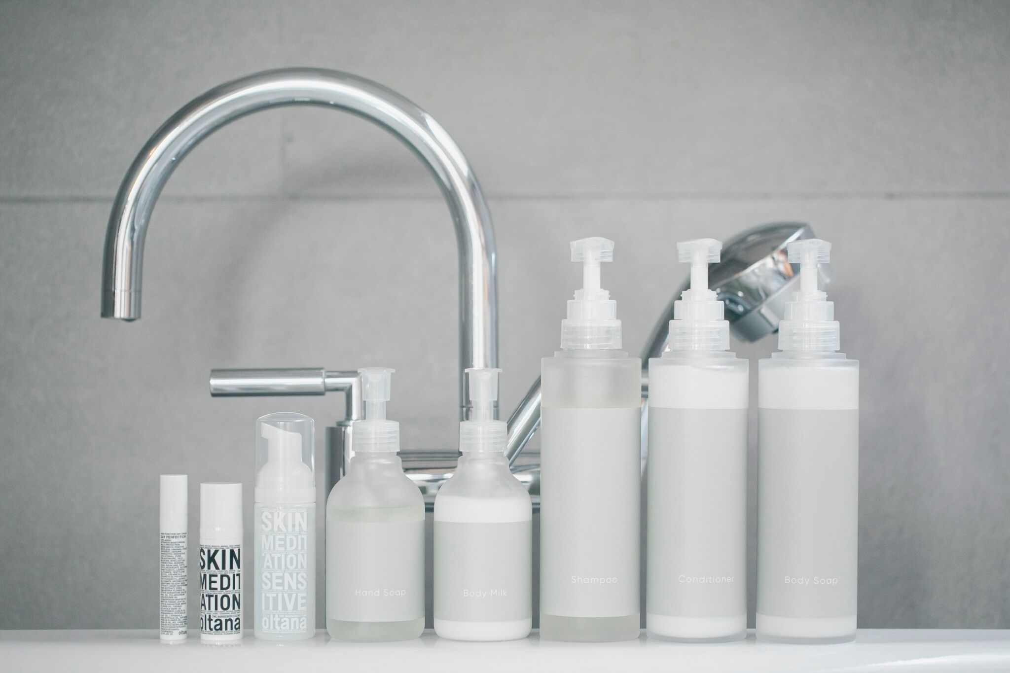 A bathroom with a modern faucet, various toiletries including body soap, shampoo, and conditioner, and a bottle labeled 'SKIN MEDIATION'.