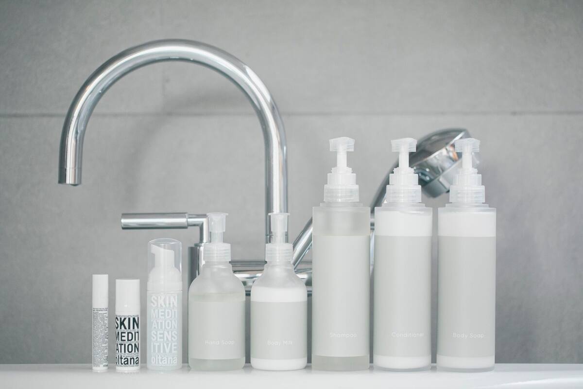 A bathroom with a modern faucet, various toiletries including body soap, shampoo, and conditioner, and a bottle labeled 'SKIN MEDIATION'.