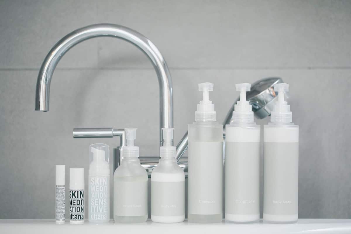 A bathroom with a modern faucet, various toiletries including body soap, shampoo, and conditioner, and a bottle labeled 'SKIN MEDIATION'.