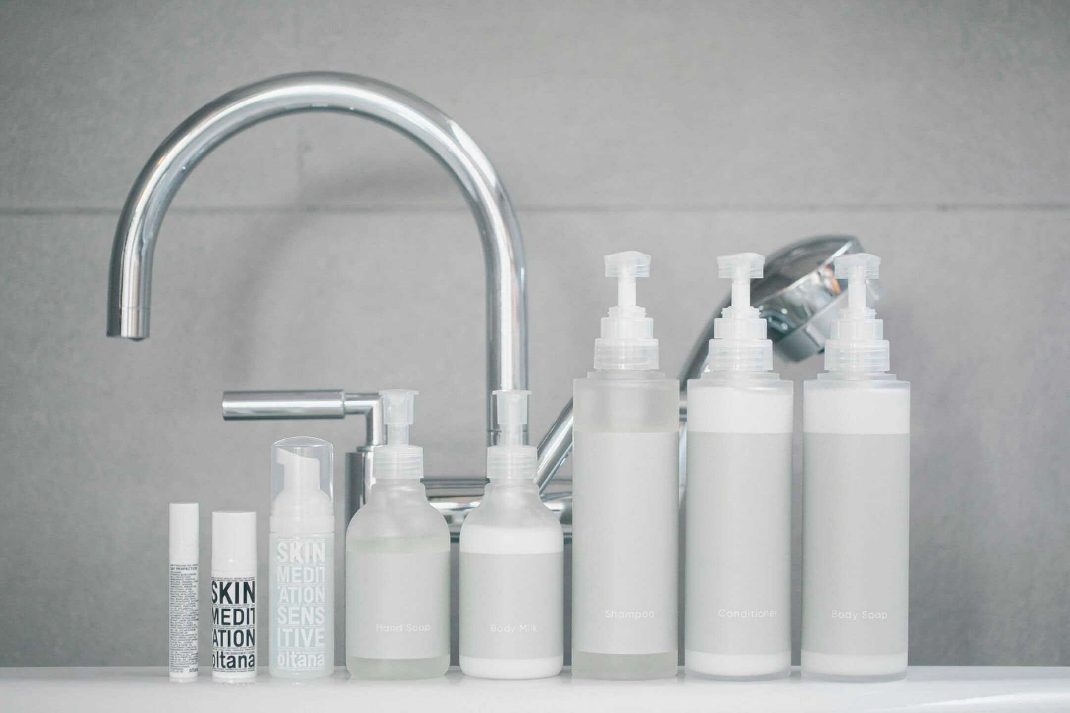 Un baño con un grifo moderno y diversos artículos de aseo, incluyendo leche corporal, champú y acondicionador.