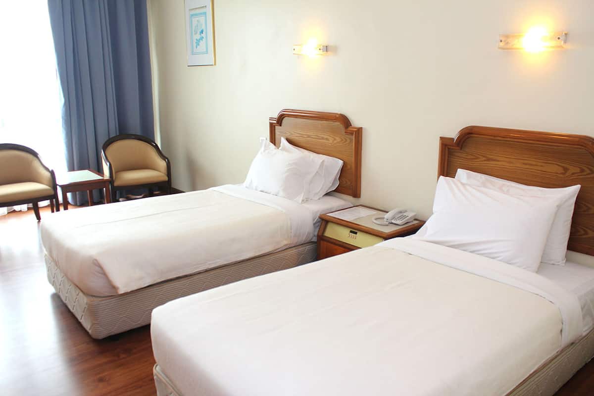 Dos camas individuales con cabeceros de madera, una mesita de noche con teléfono y una silla en una habitación de hotel.