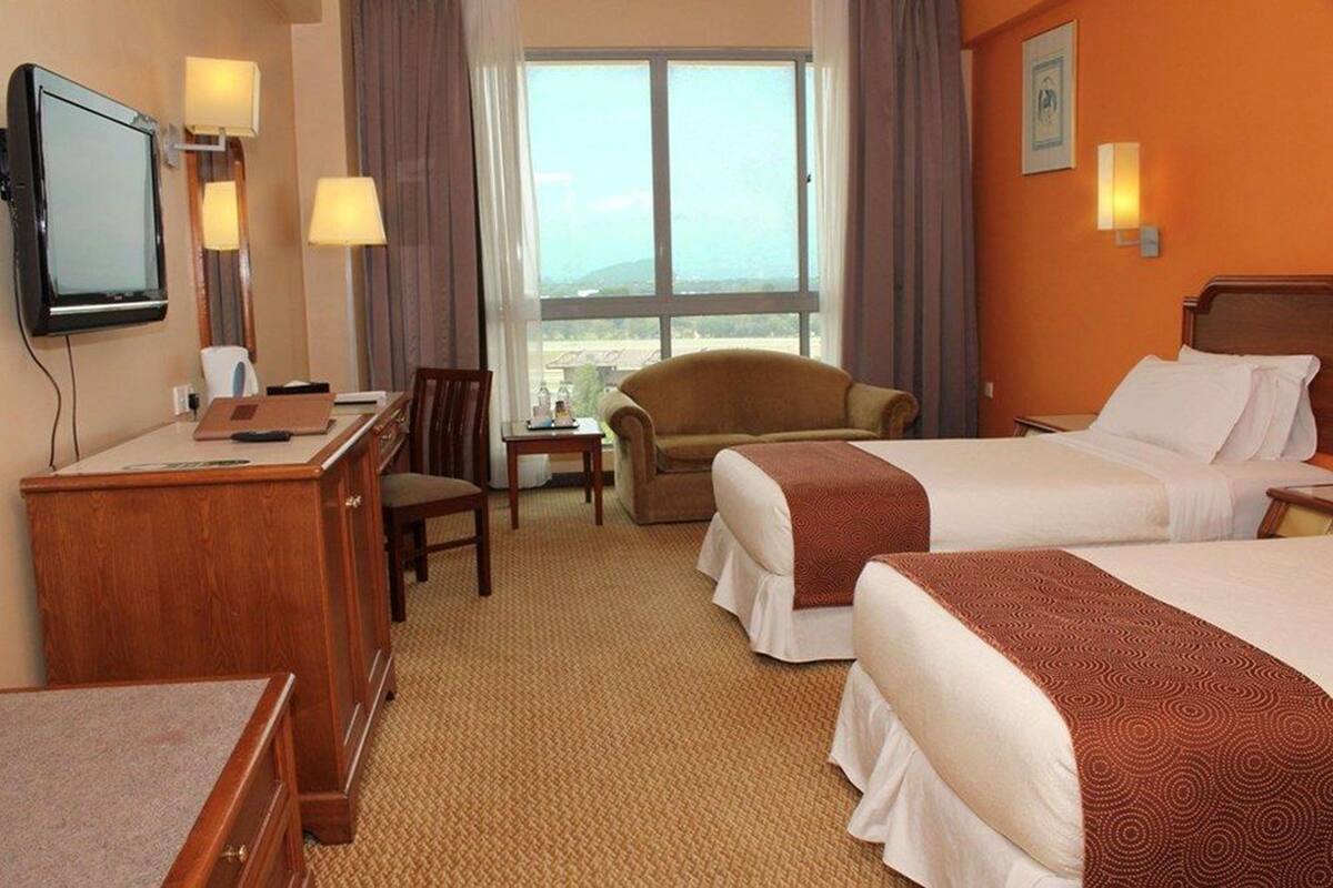 Habitación de hotel con dos camas, un escritorio, una silla, un televisor y una ventana con cortinas.