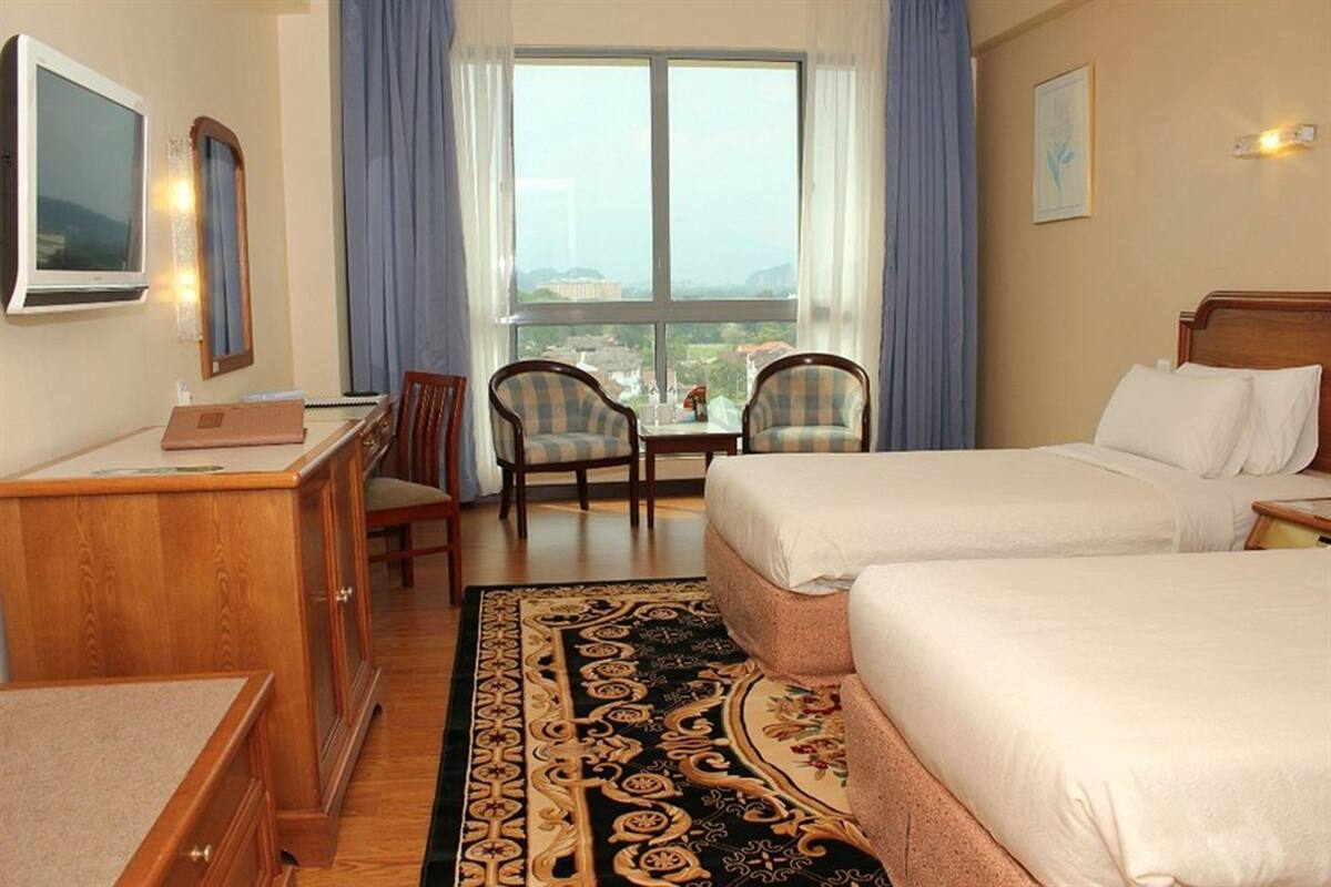 Habitación de hotel con dos camas, un escritorio, una silla, un televisor y un ventanal grande con cortinas.