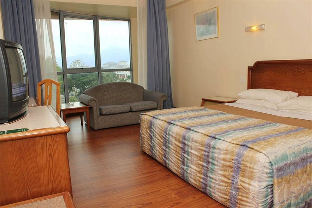 Habitación de hotel con cama, sofá, televisión y ventana con vistas a las montañas.